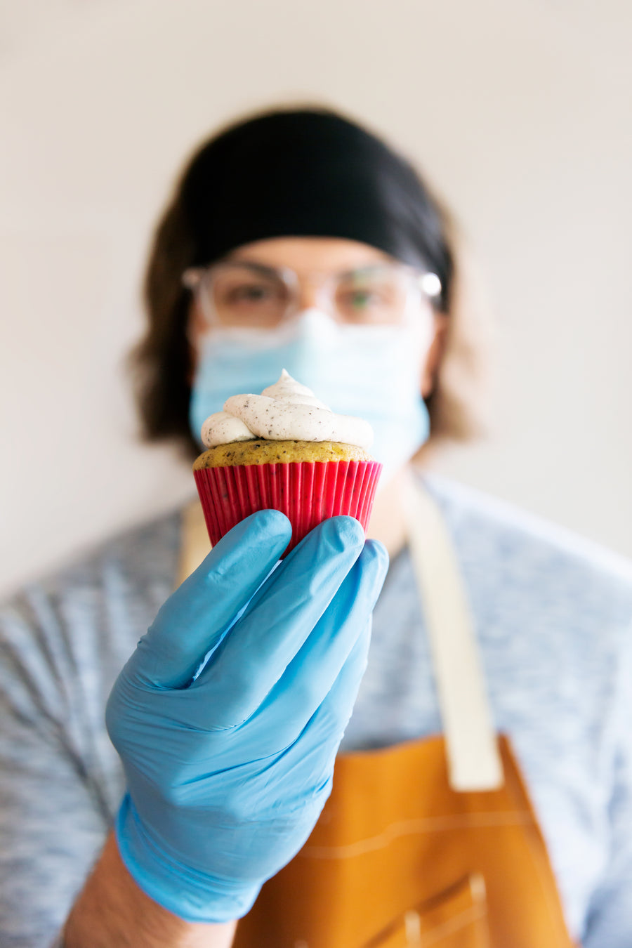 Food handler in gloves and mask holding a cupcake, illustrating safe food handling